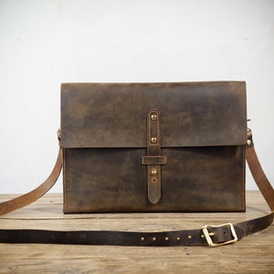May include: A brown leather messenger bag with a flap closure and a long adjustable strap. The bag has a distressed look and features a brass buckle and rivets.