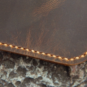 May include: Close-up of brown leather with a stitched edge. The stitching is a light brown colour.