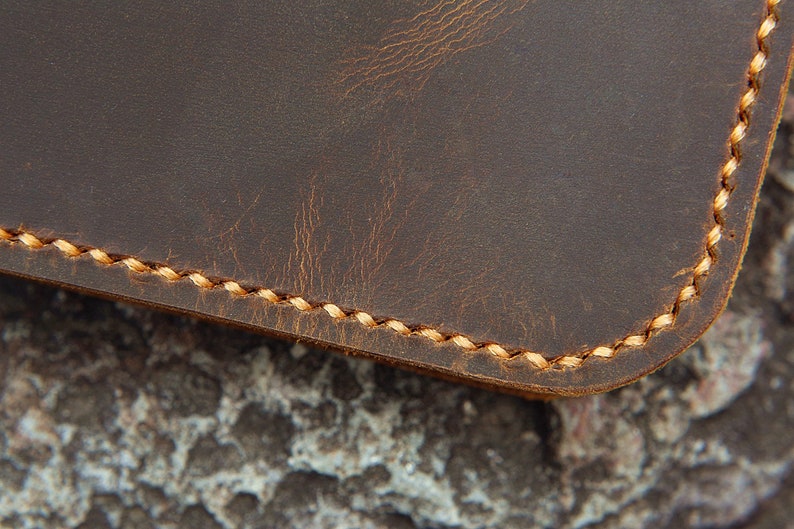 May include: Close-up of brown leather with a stitched edge. The stitching is a light brown colour.