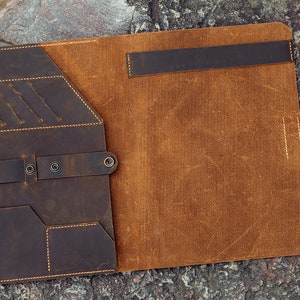 May include: A brown leather folder with multiple pockets and a flap closure. The folder is open and the inside is a lighter brown leather.