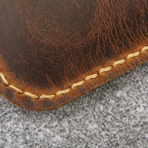 May include: Close-up of a brown leather item with a stitched edge. The stitching is a light cream color.