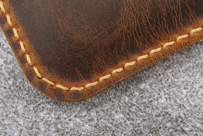 May include: Close-up of a brown leather item with a stitched edge. The stitching is a light cream color.