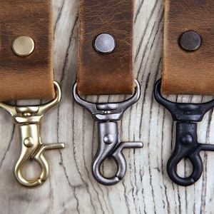 May include: Three leather keychains with different colored metal clasps. The clasps are gold, silver, and black.