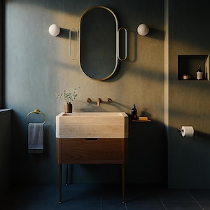 May include: A modern bathroom vanity with a stone sink and a wooden cabinet. The vanity has a gold-framed mirror and matching fixtures. A towel ring and a toilet paper holder are also visible. The walls are painted in a muted green color.