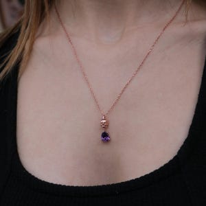 May include: A rose gold necklace with a small skull charm and a purple gemstone pendant.