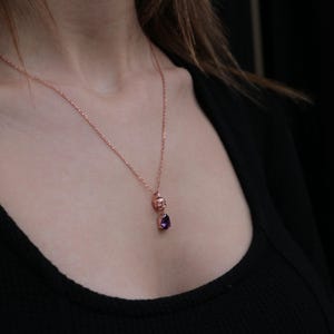 May include: A rose gold necklace with a small skull charm and a purple gemstone pendant.