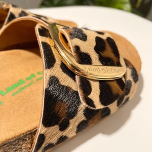 Pu&ograve; includere: Sandali con stampa leopardata con fibbia dorata e il nome del marchio "Band of Cowgirls" in rilievo sulla fibbia.