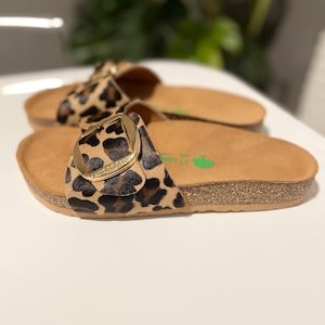 Pu&ograve; includere: Un paio di sandali marroni e neri con stampa leopardata e fibbia dorata. I sandali hanno una suola in sughero.