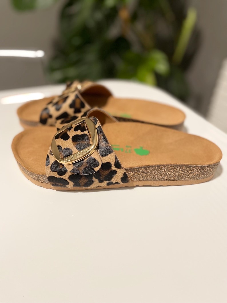 Pu&ograve; includere: Un paio di sandali marroni e neri con stampa leopardata e fibbia dorata. I sandali hanno una suola in sughero.