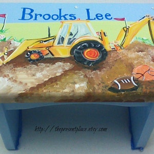 May include: A blue wooden step stool with a hand-painted design of a yellow excavator, sports balls, and the name "Brooks Lee".
