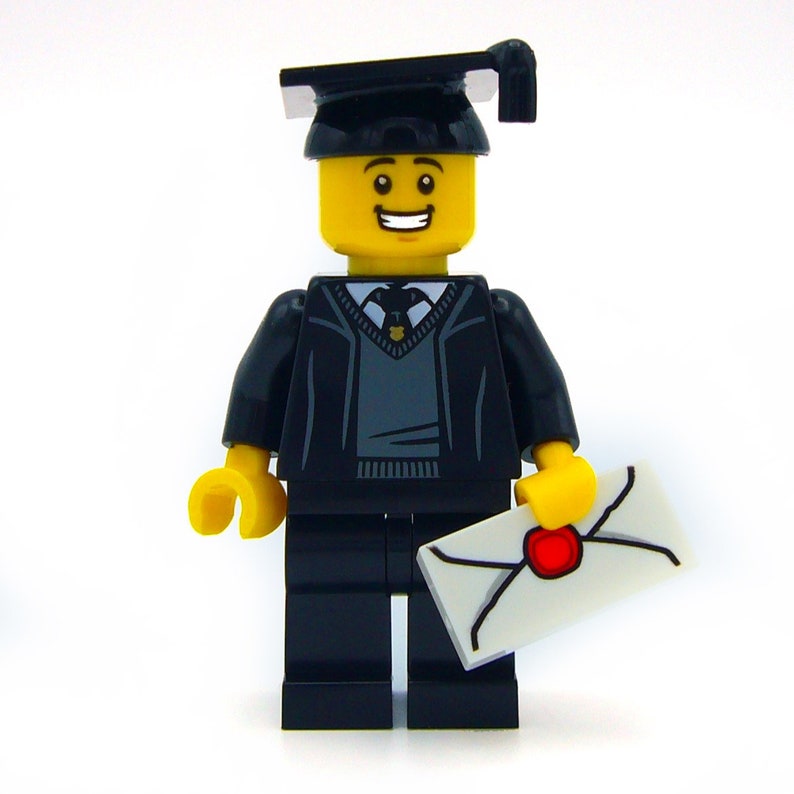 May include: A black Lego minifigure wearing a black graduation cap and gown, holding a white envelope with a red wax seal. The minifigure has a yellow face with a smile and black eyes.