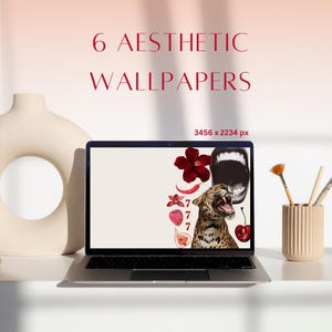 May include: A laptop computer displaying a digital collage wallpaper featuring a leopard, red flowers, cherries, and the number 7 repeated several times. The wallpaper is 3456 x 2234 pixels. The laptop is on a white surface with a white ceramic donut-shaped object and two paintbrushes in a beige container.