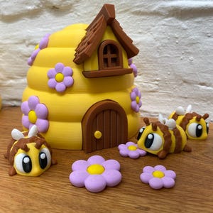Könnte beinhalten: Eine skurrile gelbe Bienenwabe mit braunem Dach, Tür und Fenster, verziert mit lila Blumen. Mehrere Cartoon-Bienen und zusätzliche lila Blumen sind um den Bienenstock verstreut.