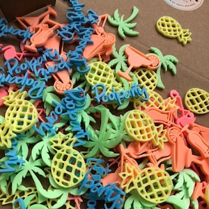 Könnte beinhalten: Eine Sammlung farbenfroher, 3D-gedruckter Dekorationen im Tropen-Stil. Das Sortiment umfasst Ananas, Palmen, Cocktailgläser und die Worte "Pool Party" in Blau. Die Dekorationen sind in Gelb-, Grün-, Orange- und Rosatönen gehalten.