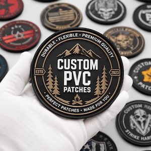 Op de afbeelding: Een verzameling zwarte, bruine en rode PVC-patches. De centrale patch, vastgehouden door een gehandschoende hand, toont de tekst "CUSTOM PVC PATCHES" met een berg- en boomontwerp. Andere patches tonen diverse ontwerpen, waaronder een schedel en een Amerikaanse vlag.