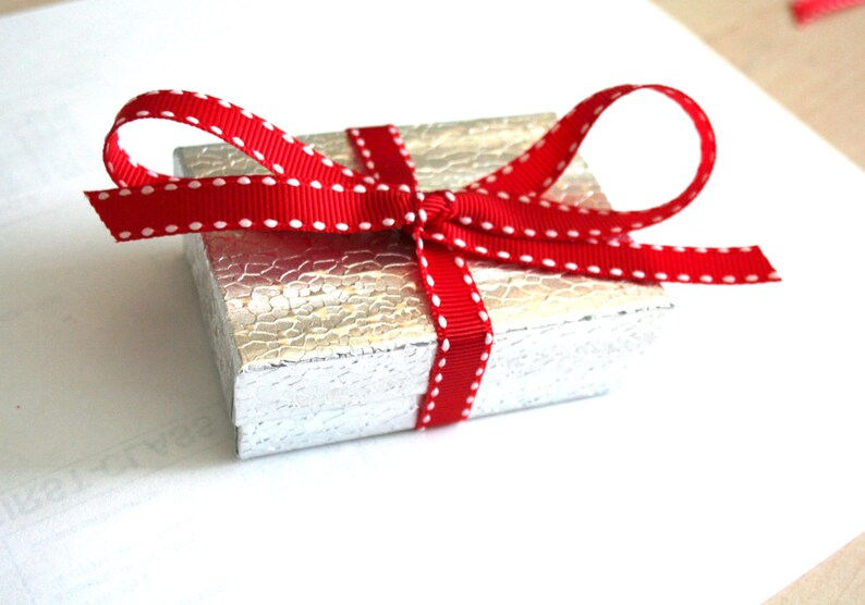 May include: A small silver gift box with a red ribbon with white polka dots tied in a bow.