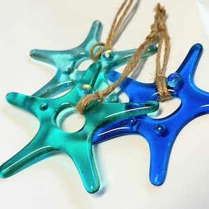 May include: Two glass starfish ornaments, one blue and one teal, hanging from a twine string.