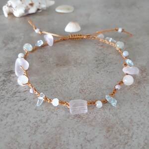 May include: A handmade bracelet featuring a macrame cord adorned with various gemstones. The bracelet includes pink, white, and light blue stones. The stones are of different shapes and sizes, adding to the unique design. The bracelet is a delicate piece of jewelry.