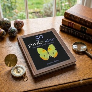 May include: A hardcover book titled 50 Physics Ideas You Really Need to Know by Joanne Baker, featuring a yellow butterfly on the cover. The book is placed on a wooden surface alongside a brass compass, a magnifying glass, and three stacked books.