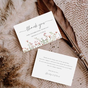 May include: Two white thank you cards with floral accents. The top card reads "thank you" in script, followed by "FOR CELEBRATING WITH US!" and a couple's names. The bottom card includes a thank you message and the couple's names.