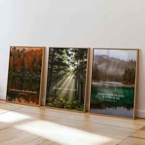 May include: Three framed landscape prints with wooden frames. The prints feature nature scenes: a forest with sunlight, a lake with fall foliage, and a misty lake. Each print has a Bible verse.
