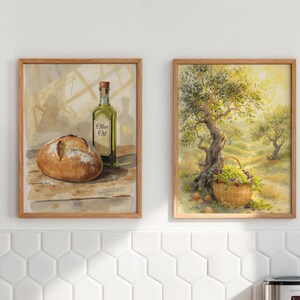 May include: Two framed watercolour paintings. The left painting depicts a loaf of bread, a bottle of olive oil, and the text "Olive Oil". The right painting shows a basket of grapes under a tree.
