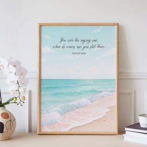 Könnte beinhalten: Ein gerahmter Druck mit einer Strandszene mit türkisfarbenem Wasser und einem sandigen Ufer. Der Himmel ist hellblau mit Wolken. Der Text lautet: „Du beherrschst das tobende Meer; wenn sich seine Wellen erheben, stillst du sie. PSALM 89:9.“