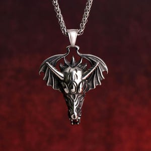May include: A silver dragon pendant necklace with a detailed design. The dragon has wings and a fierce expression. The necklace is made of a silver chain.
