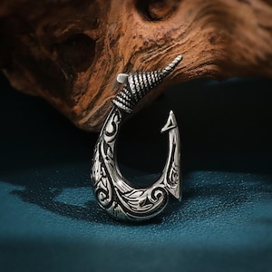 May include: A silver-toned, ornate, decorative hook pendant with a detailed floral design. The hook is curved and has a pointed tip.