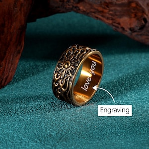 May include: A gold-colored ring with an engraved sunburst design. The ring has the words "love you" engraved on the inside. The ring is a band style and is likely made of metal.