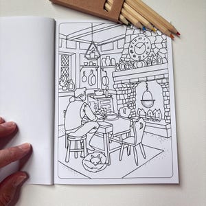 May include: A black and white coloring book page featuring a cozy interior scene with a person sitting at a wooden table, a stone fireplace with a hanging cauldron, a clock, shelves with bottles, and a sleeping fox on the floor, with colored pencils.