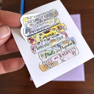 May include: A sticker sheet featuring illustrations of classic book titles, including "Northanger Abbey," "Persuasion," "Emma," "Mansfield Park," "Pride and Prejudice," and "Sense and Sensibility." Each title is displayed on a colorful, book-shaped design with related imagery.