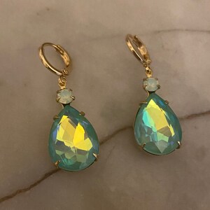 May include: A pair of gold dangle earrings with teardrop-shaped green iridescent crystals and smaller white crystals.