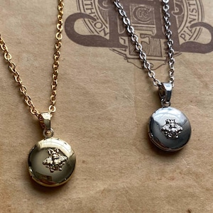 May include: Two necklaces with circular pendants, one gold and one silver. Each pendant has a small, intricate design. They are displayed on a vintage paper background with text, including 'HENRY LEMOINE &'.