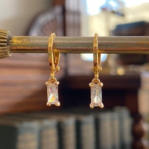 May include: A pair of gold hoop earrings with a dangling rectangular clear crystal.