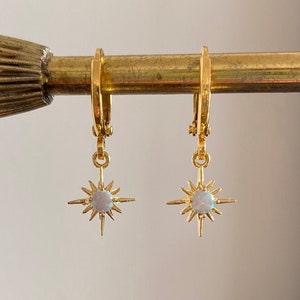 May include: Gold hoop earrings with a dangling star charm featuring a white opal stone.