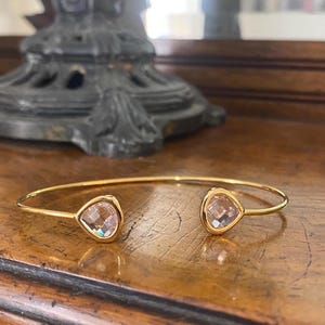 May include: A gold bangle bracelet with two clear teardrop-shaped crystals.