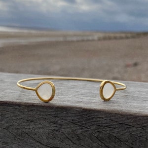 Può includere: Un braccialetto rigido in oro con due pietre bianche a forma di lacrima.