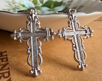 May include: A pair of silver-toned metal cross pendants featuring intricate filigree scrollwork and a textured center panel. Each cross has a small loop at the top for attachment, showcasing a detailed, ornate design with pointed fleur-de-lis accents.