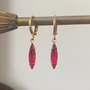May include: A pair of gold hoop earrings with dangling red teardrop-shaped crystals.
