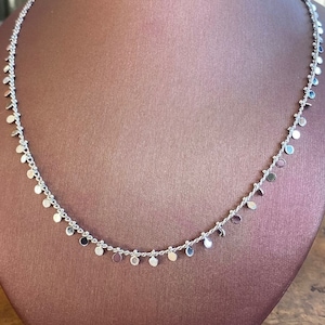 Puede incluir: Un collar de plata con pequeños colgantes redondos de plata. El collar está en un busto de maniquí marrón.