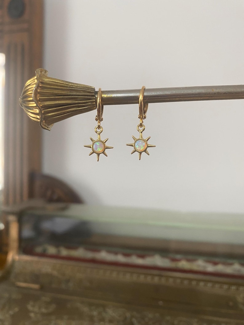 May include: Gold hoop earrings with a dangling star charm featuring a white opal gemstone.