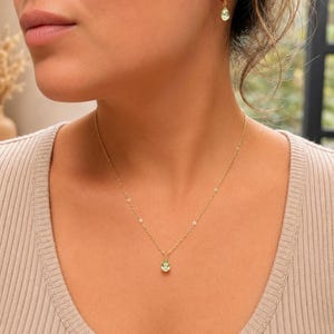 May include: A gold chain necklace featuring a small, light green, teardrop-shaped pendant. The set includes matching gold hoop earrings, each adorned with a single, light green, teardrop-shaped charm that hangs from the bottom of the hoop.