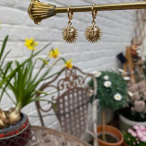 Op de afbeelding: Gouden creolen met een zon hanger. De zon hanger heeft een gezicht en stralen.