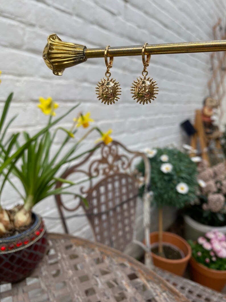 Op de afbeelding: Gouden creolen met een zon hanger. De zon hanger heeft een gezicht en stralen.