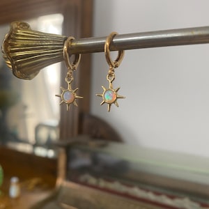 May include: Gold hoop earrings with a dangling star charm featuring a white opal gemstone.