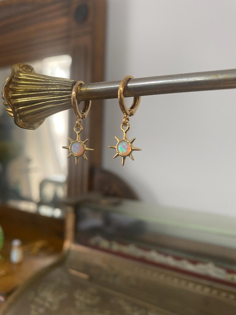 May include: Gold hoop earrings with a dangling star charm featuring a white opal gemstone.