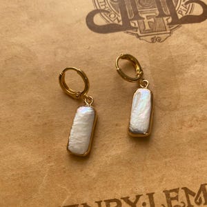 May include: A pair of gold hoop earrings with a white rectangular pearl pendant hanging from each hoop.