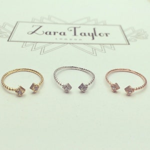 Op de afbeelding: Drie open ringen in goud, zilver en roségoud, elk met een ruitvormig accent met een kleine, heldere steen. De ringen worden gepresenteerd op een witte ondergrond met het Zara Taylor London logo op de achtergrond.