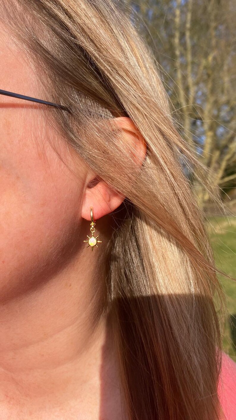 May include: Gold hoop earrings with a small sun charm featuring a yellow opal stone.